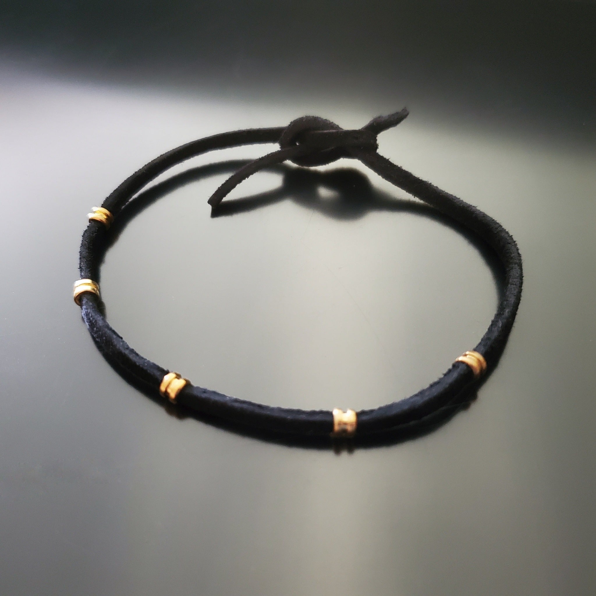 black bracelet made from a suede cord and gold coloured guitar string ballends