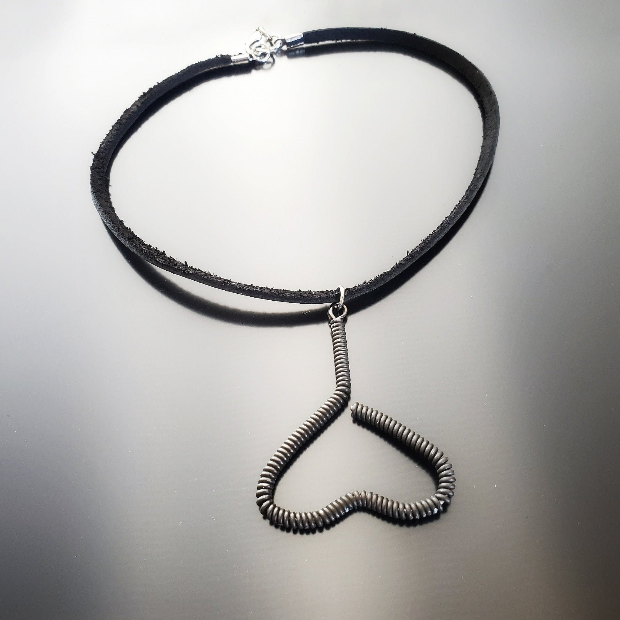 necklace - pendant is in the shape of an upside down heart and is made from a black upcycled piano string - pendant hangs off a black leather cord