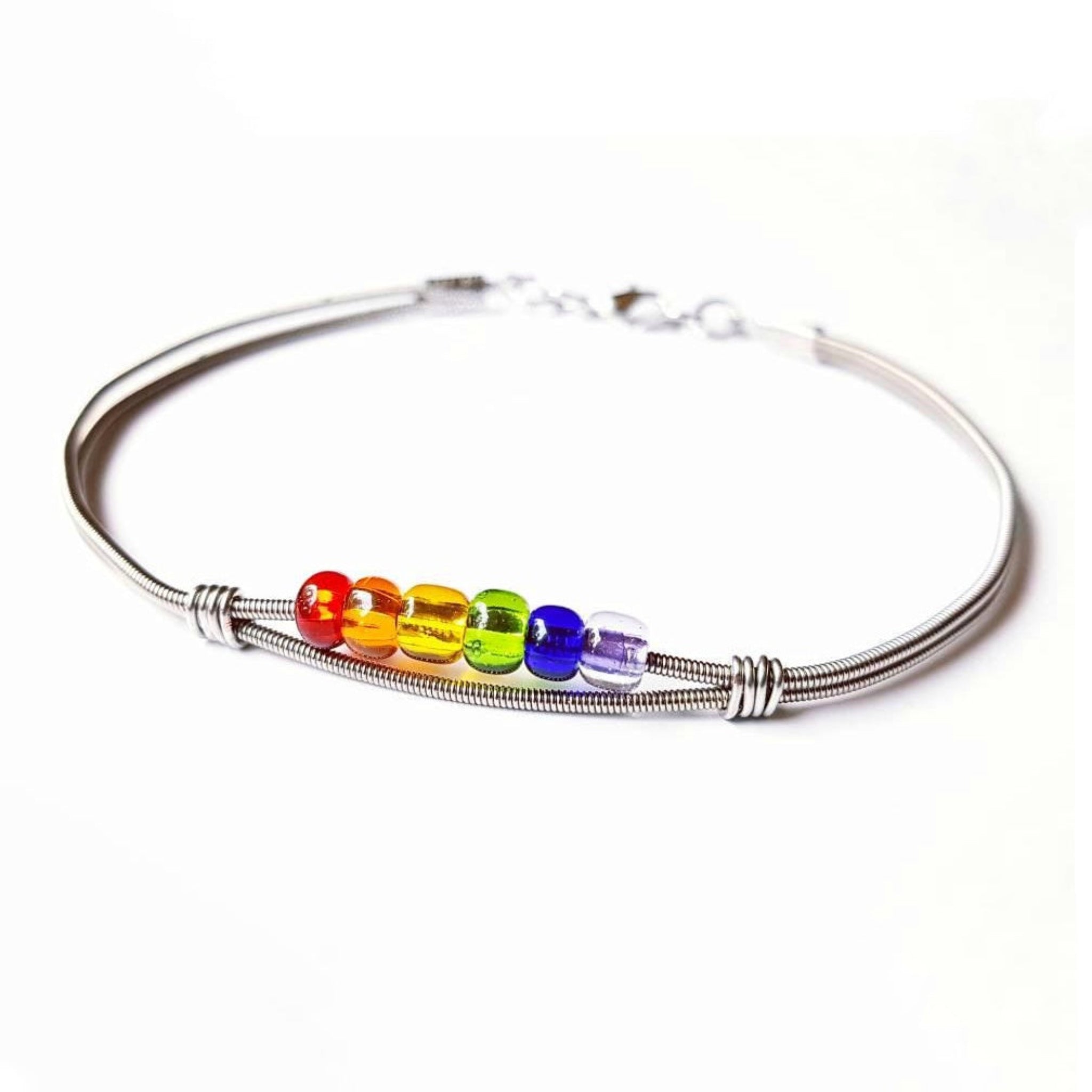 clasp style bracelet made from an upcycled guitar string - 6 glass beads represent the colours of the LGBTQ flag (red, orange, yellow, green, blue and purple) - white background