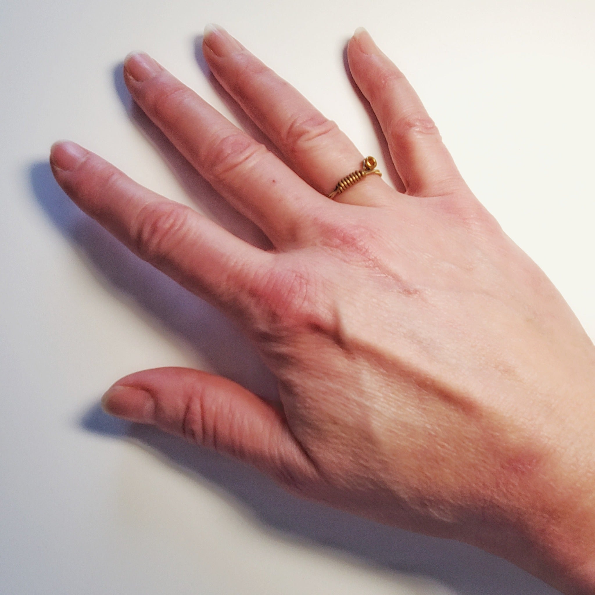 woman's hand wearing a gold coloured guitar string ring - white background