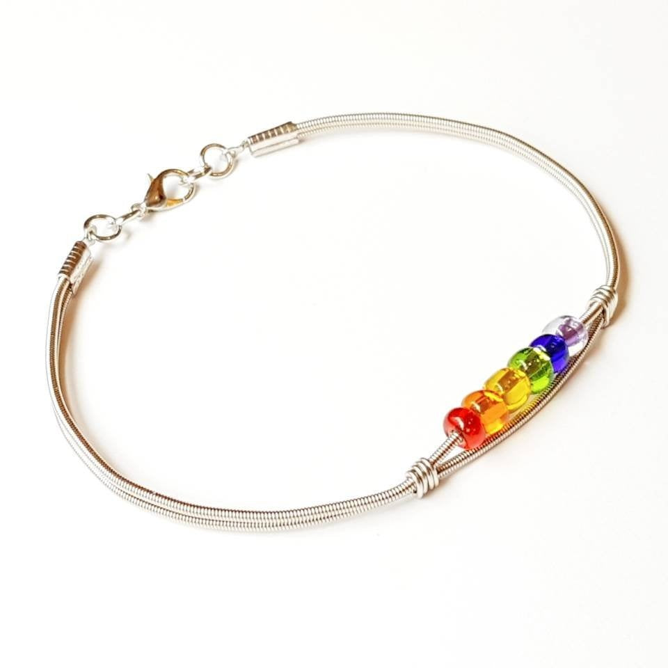 clasp style bracelet made from an upcycled guitar string - 6 glass beads represent the colours of the LGBTQ flag (red, orange, yellow, green, blue and purple) - white background