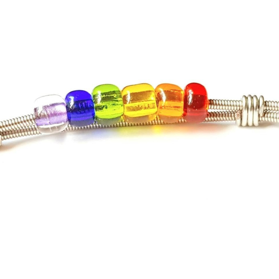 close-up of a clasp style bracelet made from an upcycled guitar string - 6 glass beads represent the colours of the LGBTQ flag (red, orange, yellow, green, blue and purple) - white background