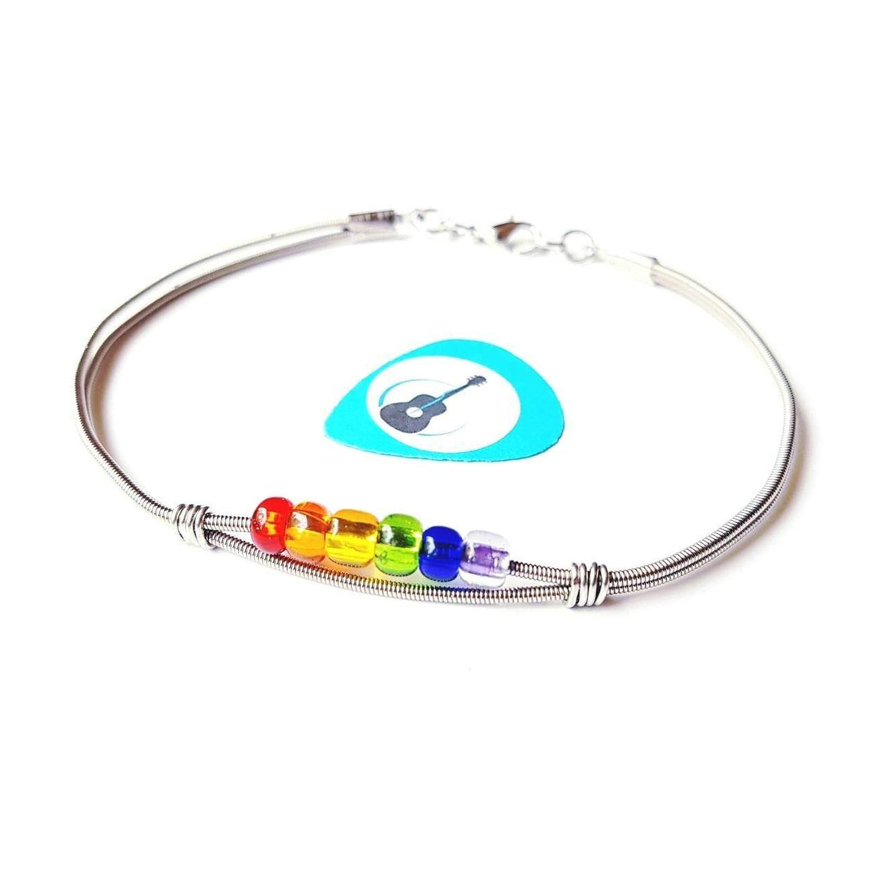 clasp style bracelet made from an upcycled guitar string - 6 glass beads represent the colours of the LGBTQ flag (red, orange, yellow, green, blue and purple) - blue guitar pick with an image of a black guitar - white background