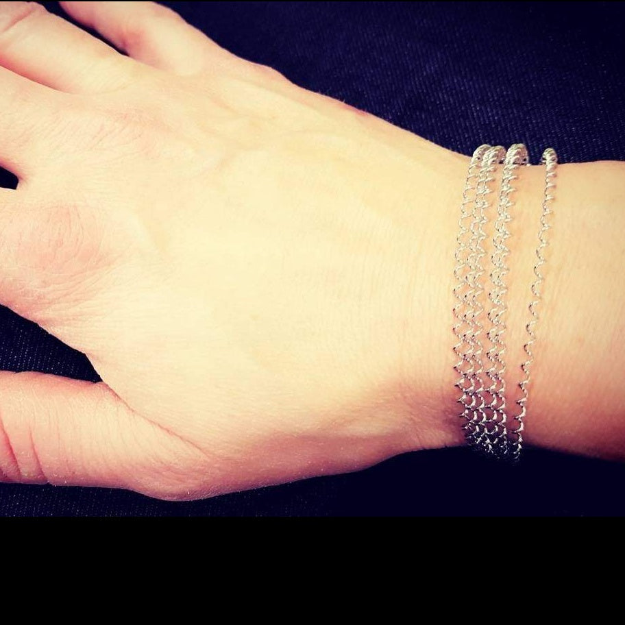 woman's hand and wrist - she is wearing a silver coloured clasp style bracelet made from a series of upcycled snare drum strings 