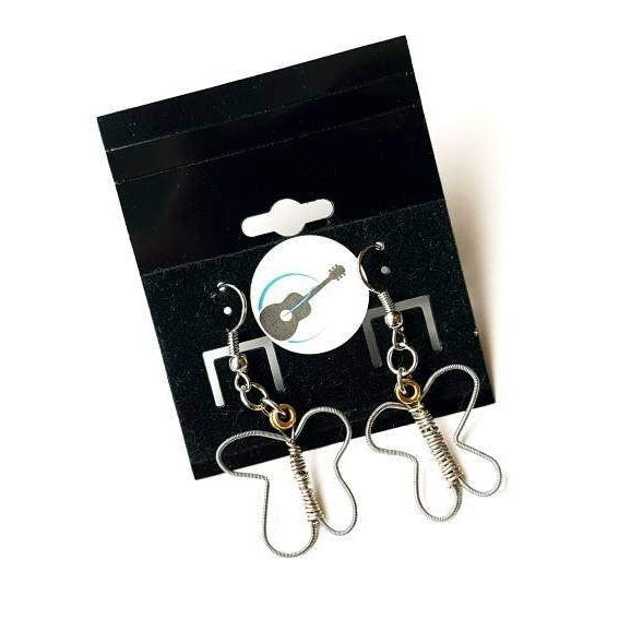 a pair of earrings made from upcycled guitar strings shaped into butterflies - the earrings hang on a black jewelry card which has a round white sticker with a picture of a black guitar and a blue circle - white background