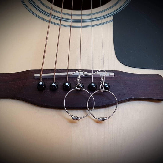 small hoop style earrings made from upcycled guitar strings hanging from the bridge of a beige guitar