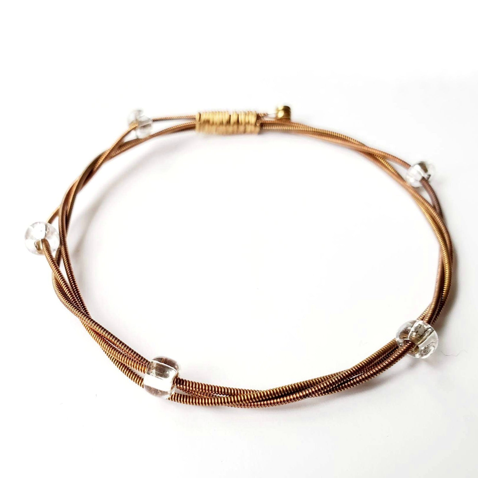 copper coloured bangle style bracelet made from an upcycled guitar string and clear glass beads - white background