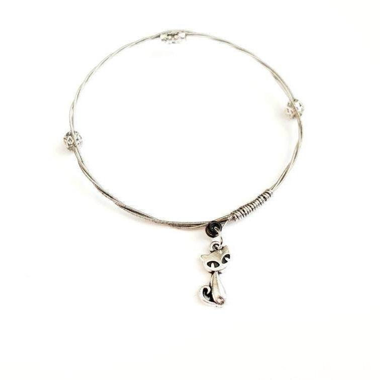 a silver coloured bangle style bracelet made from an upcycled guitar string on which a silver coloured cat shaped pendant hangs -white background