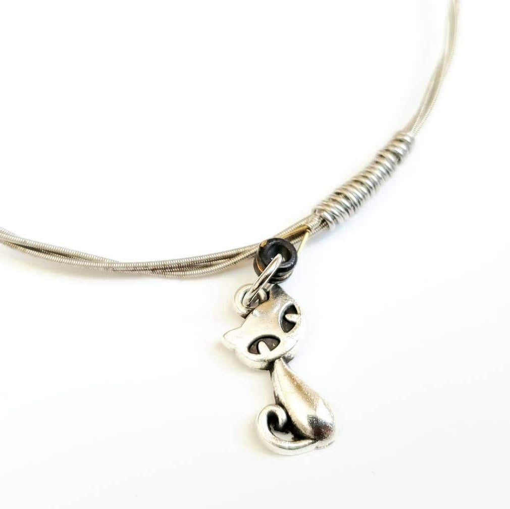 closeup of a silver coloured bangle style bracelet made from an upcycled guitar string on which a silver coloured cat shaped pendant hangs -white background