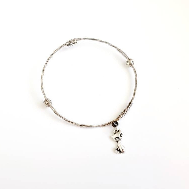 a silver coloured bangle style bracelet made from an upcycled guitar string on which a silver coloured cat shaped pendant hangs -white background
