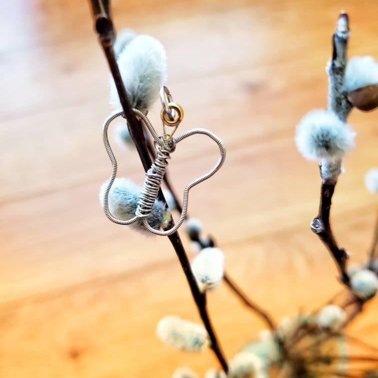 a pendant made from an upcycled guitar string shaped into a butterfly hangs on a pussywillow branch - yellow background