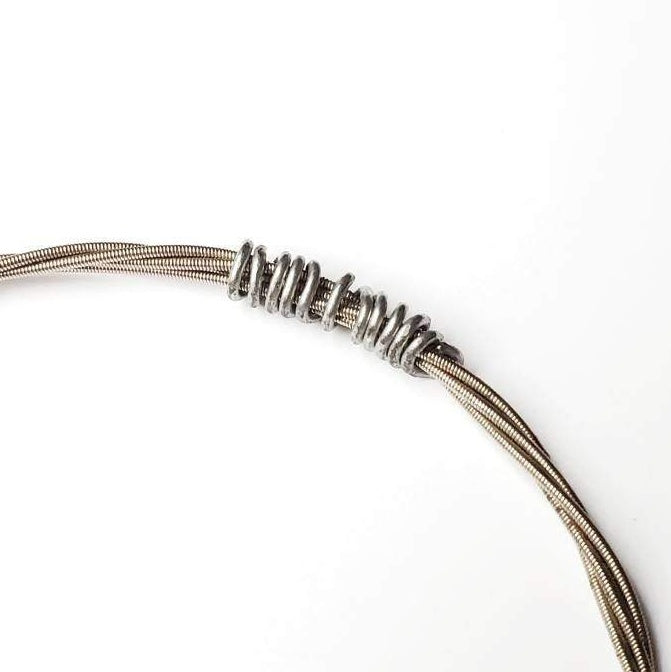 close-up of part of a bracelet made from an upcycled guitar string held by a silver coloured wire - white background