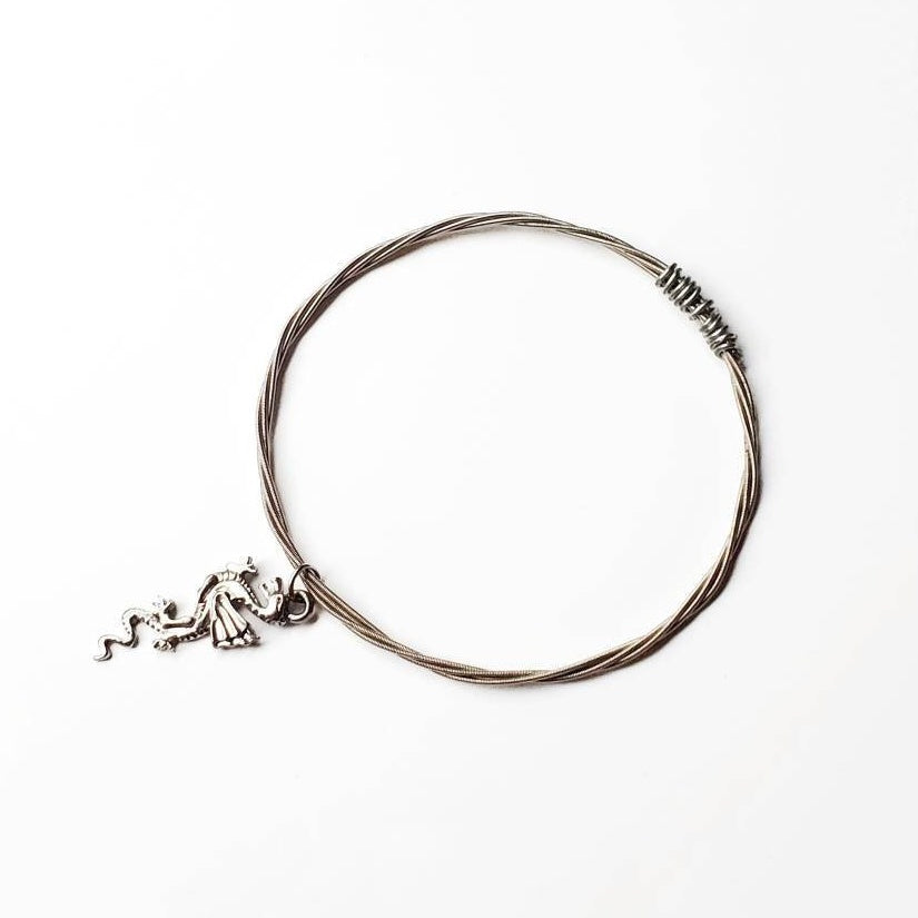 silver coloured bangle style bracelet made from an upcycled guitar string with a dragon shaped pendant - white background