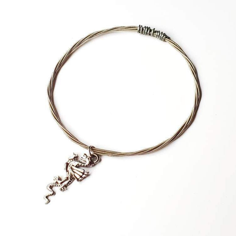 silver coloured bangle style bracelet made from an upcycled guitar string with a dragon shaped pendant - white background