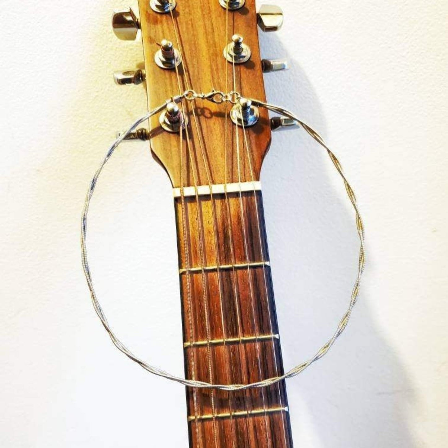 a silver chain style necklace made from braided guitar strings hangs from a wood guitar neck