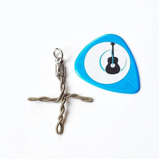 a cross shaped pendant made from an upcycled guitar string -next to it is a blue guitar pick with a white circle and the picture of a black guitar - white background