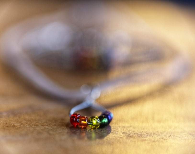 close-up of a necklace made from an upcycled guitar string - 6 glass beads represent the colours of the LGBTQ flag (red, orange, yellow, green, blue and purple) and a beige suede cord 