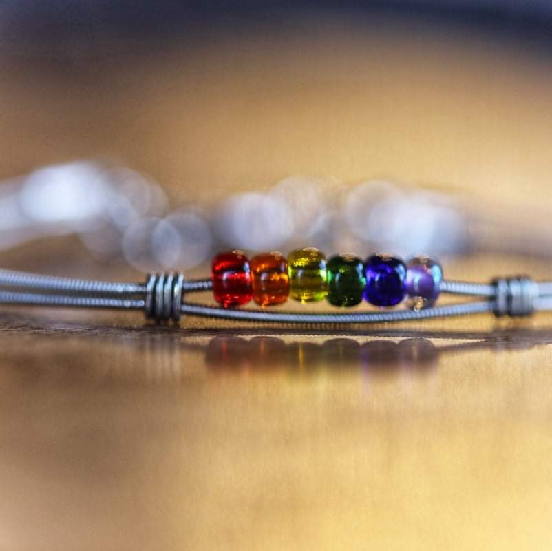 close-up of a clasp style bracelet made from an upcycled guitar string - 6 glass beads represent the colours of the LGBTQ flag (red, orange, yellow, green, blue and purple) 