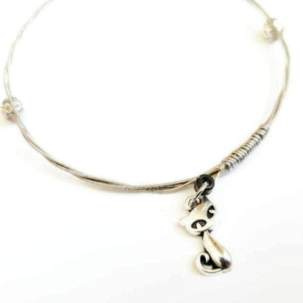 a silver coloured bangle style bracelet made from an upcycled guitar string on which a silver coloured cat shaped pendant hangs -white background